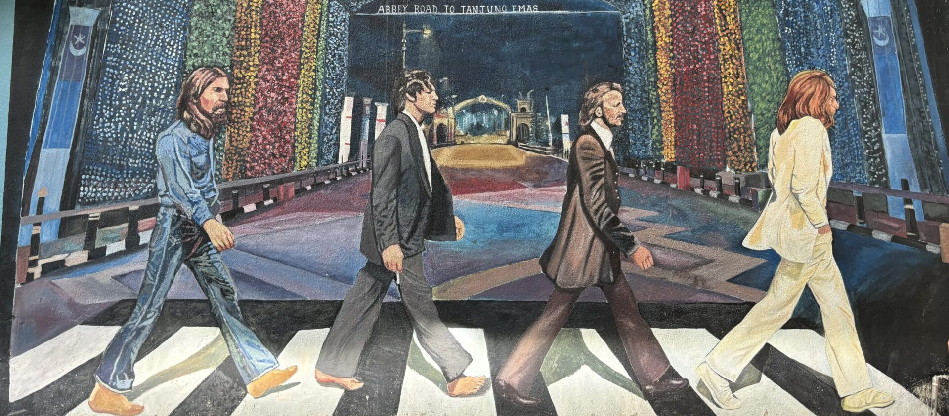 A wall mural featuring four men dressed in suits walking on a black and white crossing, similar to The Beatles iconic image.